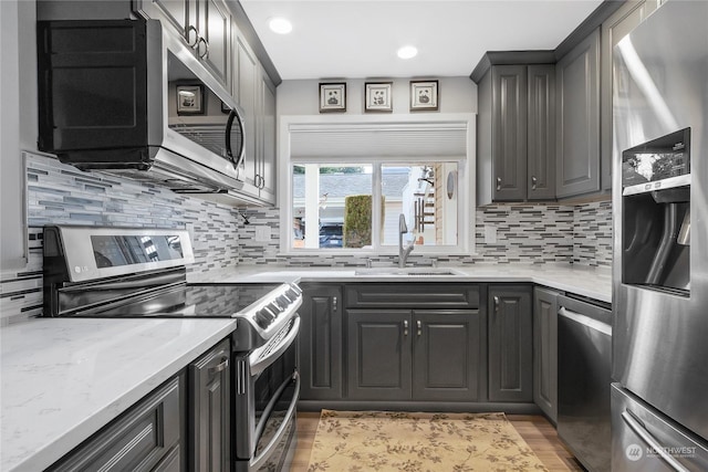 kitchen with sink, stainless steel appliances, light stone counters, and tasteful backsplash