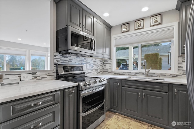 kitchen with appliances with stainless steel finishes, sink, backsplash, light stone counters, and light hardwood / wood-style flooring