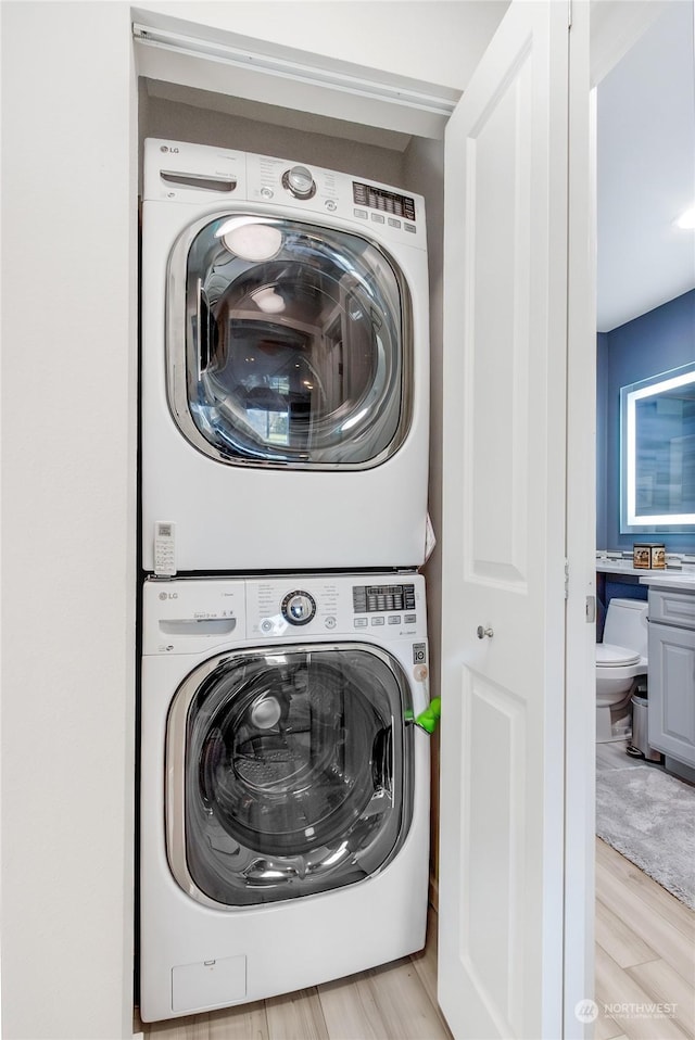 laundry room with stacked washing maching and dryer and light hardwood / wood-style flooring