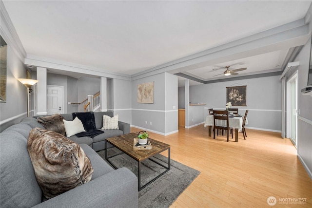 living area featuring light wood finished floors, a ceiling fan, stairs, and baseboards