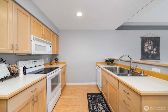 kitchen featuring light brown cabinetry, a sink, tile countertops, white appliances, and a peninsula