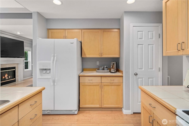 kitchen with white appliances, tile countertops, light brown cabinets, light wood finished floors, and a fireplace