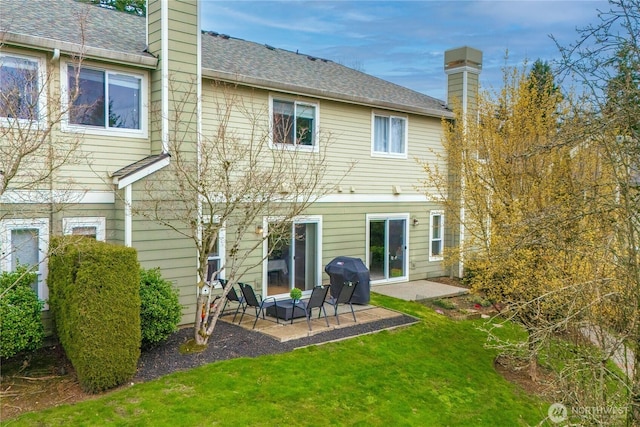 rear view of house with a patio area, a lawn, a chimney, and a shingled roof