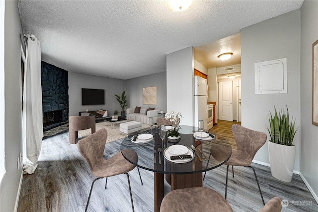 dining area featuring a textured ceiling, light hardwood / wood-style flooring, and a fireplace