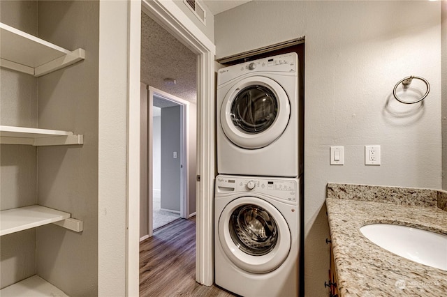 clothes washing area featuring sink, light hardwood / wood-style flooring, stacked washer / dryer, and a textured ceiling