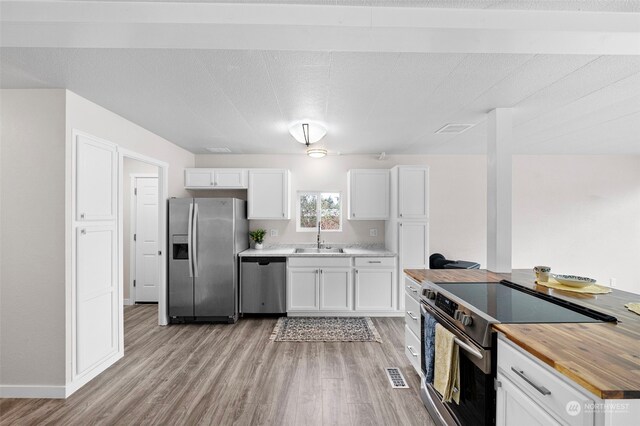 kitchen featuring sink, white cabinets, butcher block countertops, light hardwood / wood-style floors, and stainless steel appliances