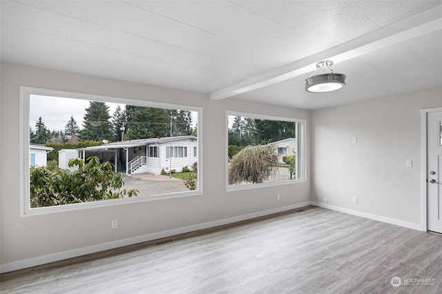 empty room with beamed ceiling, light hardwood / wood-style flooring, and plenty of natural light