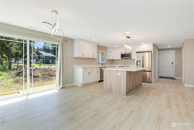 kitchen featuring appliances with stainless steel finishes, light hardwood / wood-style floors, white cabinets, a kitchen island, and decorative light fixtures