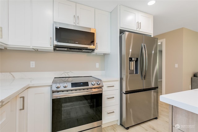 kitchen with light stone counters, stainless steel appliances, white cabinets, and light wood-type flooring