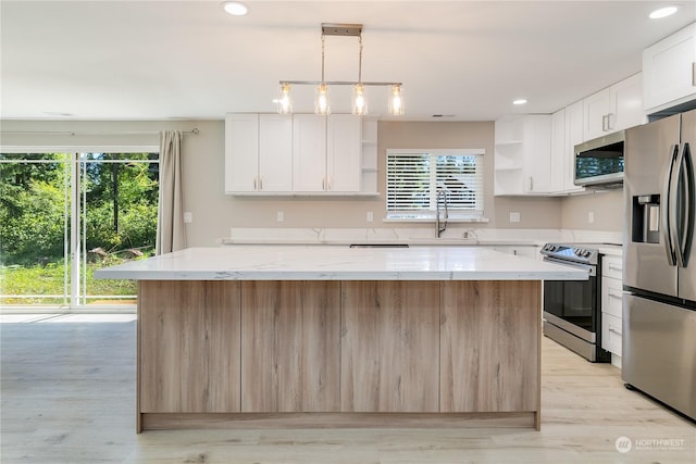 kitchen with stainless steel appliances, white cabinetry, a kitchen island, and light stone countertops