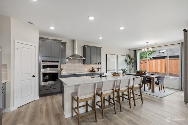 kitchen featuring sink, a center island with sink, wall chimney exhaust hood, and gray cabinets