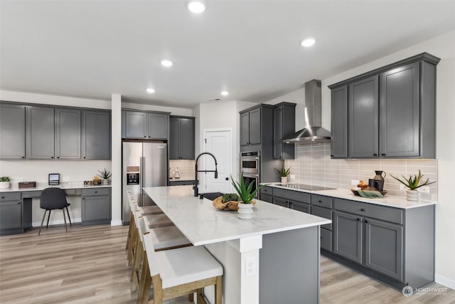 kitchen with wall chimney range hood, stainless steel appliances, a center island with sink, and gray cabinets