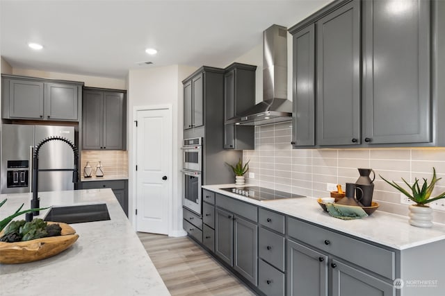 kitchen with light hardwood / wood-style flooring, appliances with stainless steel finishes, wall chimney exhaust hood, sink, and gray cabinets