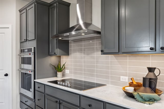 kitchen featuring wall chimney range hood, gray cabinetry, black electric cooktop, and tasteful backsplash