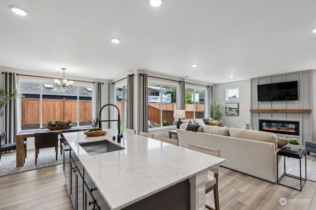 kitchen featuring hanging light fixtures, sink, light stone counters, a fireplace, and a kitchen island with sink