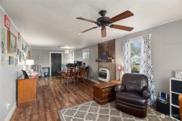 living room featuring crown molding, ceiling fan, heating unit, a large fireplace, and dark hardwood / wood-style flooring