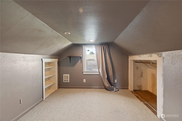 bonus room featuring carpet floors, vaulted ceiling, heating unit, and a textured ceiling