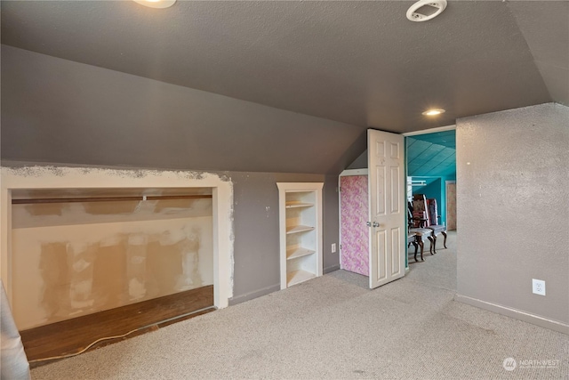 bonus room with lofted ceiling, built in shelves, carpet floors, and a textured ceiling