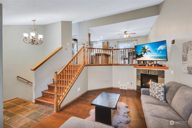 living room featuring ceiling fan with notable chandelier, dark hardwood / wood-style flooring, and a tiled fireplace