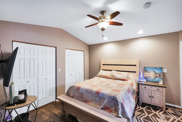 bedroom with ceiling fan, vaulted ceiling, dark hardwood / wood-style floors, and two closets