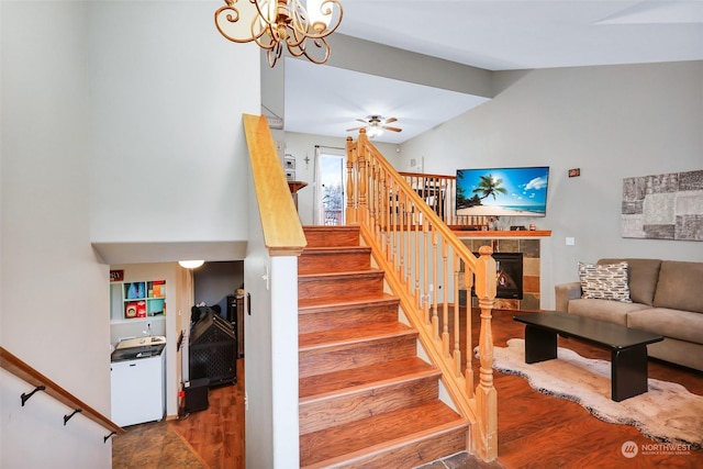 stairs with ceiling fan with notable chandelier, a tile fireplace, and lofted ceiling