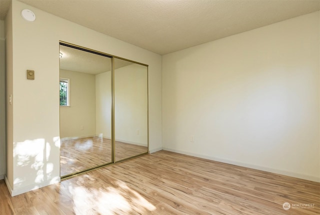 unfurnished bedroom featuring light hardwood / wood-style flooring, a textured ceiling, and a closet