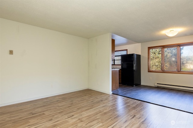 unfurnished living room featuring a baseboard heating unit, a textured ceiling, and light hardwood / wood-style floors