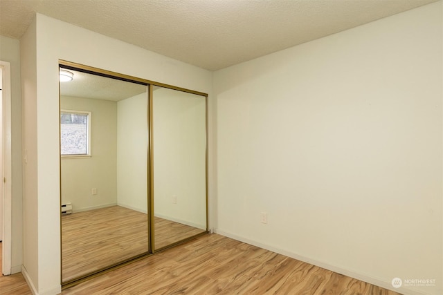 unfurnished bedroom featuring baseboard heating, a textured ceiling, a closet, and light hardwood / wood-style flooring