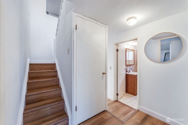 stairway with sink, hardwood / wood-style flooring, and a textured ceiling