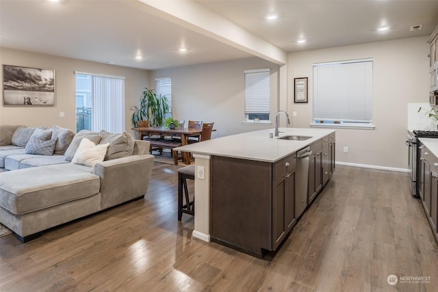 kitchen featuring dark brown cabinetry, appliances with stainless steel finishes, light hardwood / wood-style floors, sink, and a kitchen island with sink