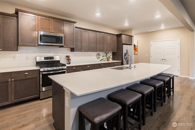 kitchen featuring hardwood / wood-style floors, appliances with stainless steel finishes, dark brown cabinetry, and a kitchen island with sink