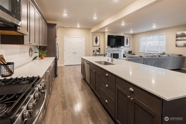 kitchen featuring hardwood / wood-style floors, dark brown cabinetry, stainless steel appliances, sink, and a center island with sink