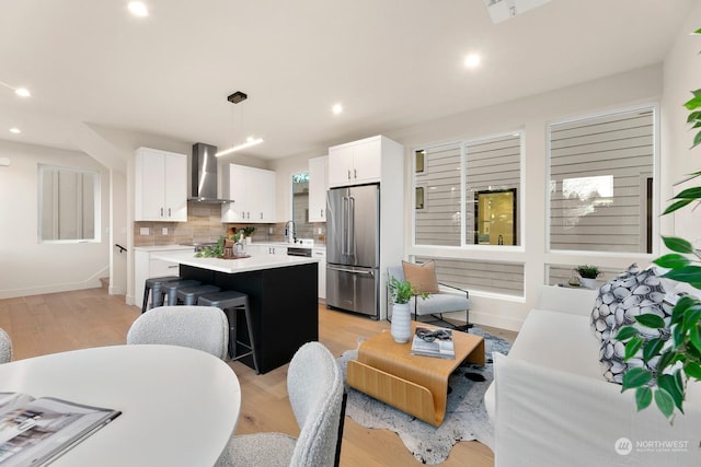 kitchen with pendant lighting, wall chimney range hood, high end fridge, white cabinetry, and a kitchen island