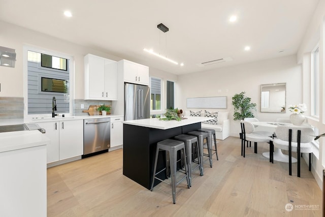 kitchen with white cabinetry, decorative light fixtures, stainless steel appliances, and a center island