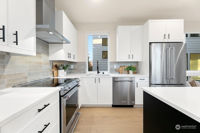 kitchen with wall chimney range hood, sink, appliances with stainless steel finishes, backsplash, and white cabinets