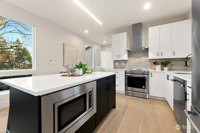 kitchen featuring white cabinetry, a center island, stainless steel appliances, light wood-type flooring, and wall chimney exhaust hood