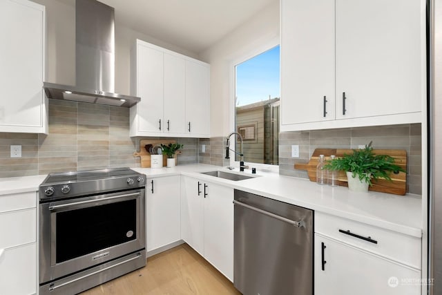 kitchen featuring stainless steel appliances, sink, wall chimney range hood, and white cabinets