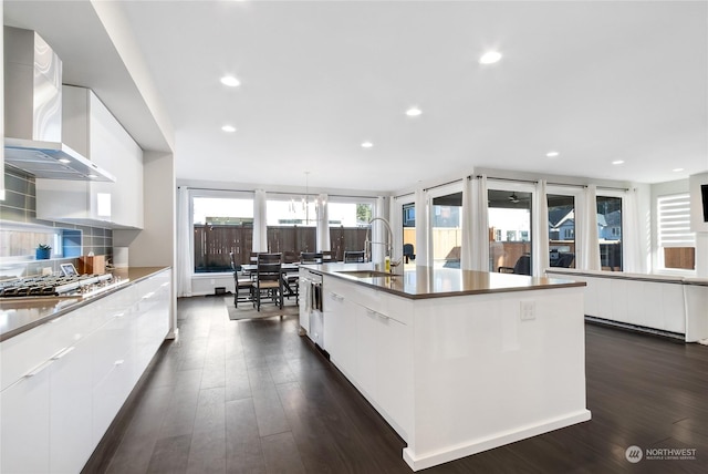 kitchen featuring sink, white cabinets, wall chimney range hood, an island with sink, and stainless steel appliances