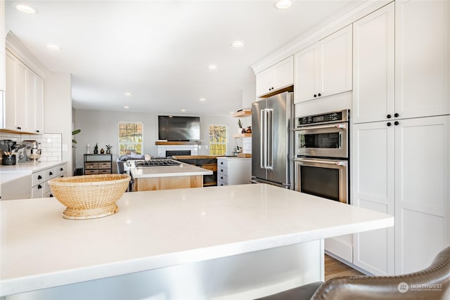 kitchen featuring white cabinetry, stainless steel appliances, a center island, tasteful backsplash, and a kitchen bar