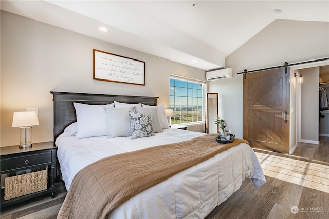 bedroom featuring a walk in closet, wood-type flooring, a wall mounted AC, vaulted ceiling, and a barn door