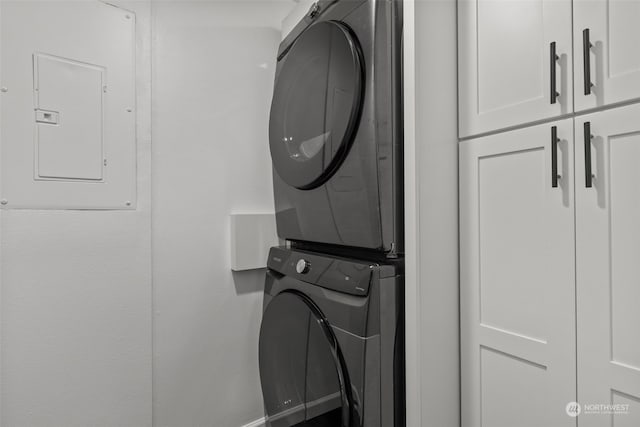 clothes washing area featuring cabinets, electric panel, and stacked washer and dryer