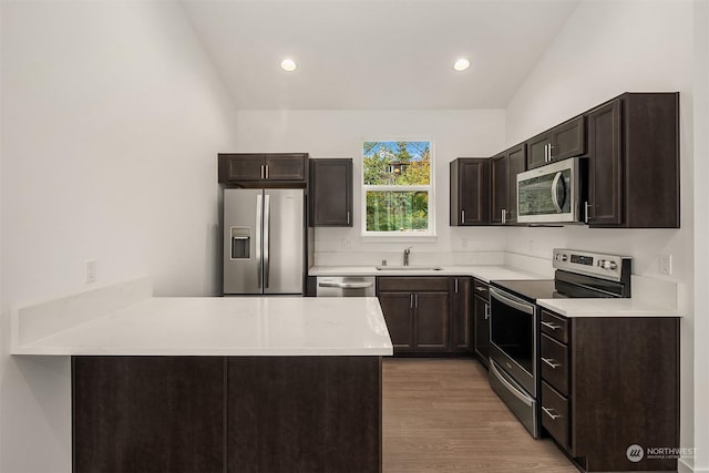 kitchen with lofted ceiling, sink, stainless steel appliances, dark brown cabinetry, and light wood-type flooring