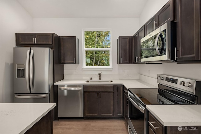 kitchen with dark brown cabinetry, sink, stainless steel appliances, and light wood-type flooring