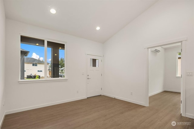 unfurnished room featuring hardwood / wood-style flooring, lofted ceiling, plenty of natural light, and a wall unit AC