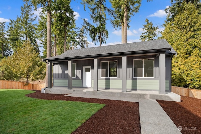 view of front facade featuring board and batten siding, fence, roof with shingles, a front yard, and covered porch