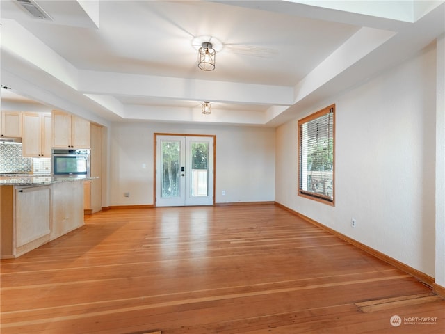 unfurnished living room featuring a raised ceiling, french doors, and light wood-type flooring