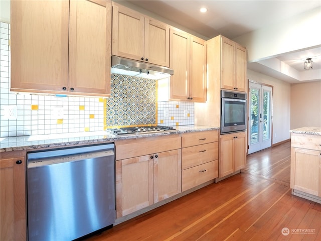 kitchen featuring light brown cabinets, appliances with stainless steel finishes, tasteful backsplash, light stone counters, and light hardwood / wood-style floors