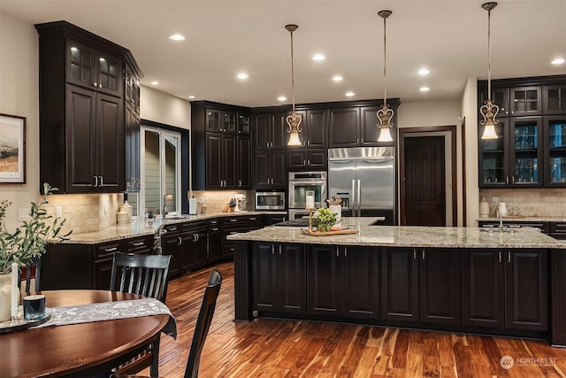 kitchen featuring a kitchen island with sink, pendant lighting, decorative backsplash, and built in appliances