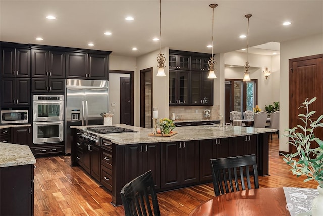 kitchen with pendant lighting, dark hardwood / wood-style flooring, stainless steel appliances, and a kitchen island with sink