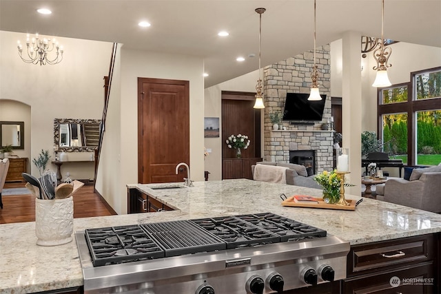 kitchen with pendant lighting, a stone fireplace, sink, stainless steel gas cooktop, and light stone counters